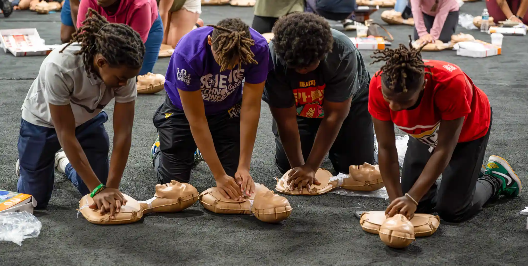 Four youth each practicing CPR on a mini manikin.